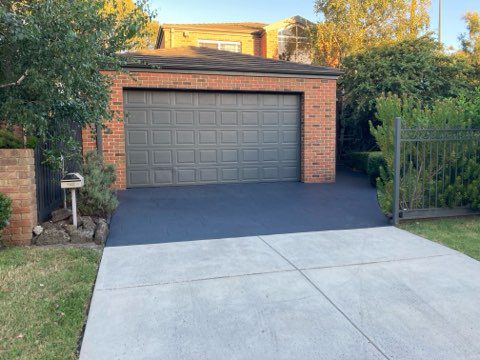 Freshly resurfaced dark grey concrete driveway leading to a brick garage with a modern finish.