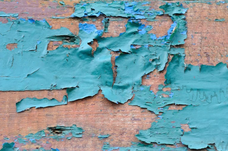 A close-up of peeling green and blue paint on a wooden surface.
